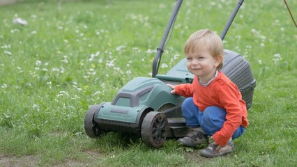 Amusing baby child play with lawn mower wheel, blond hair toddler enjoy real toy