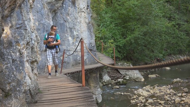 Father baby wearing passing on wooden bridge above mountain river, free parent