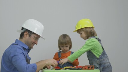 Man with two little helpers equipped, protection helmet and overall construct