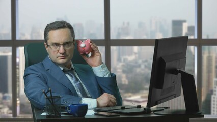 Businessman with suit sit on chair at office and look at piggy bank