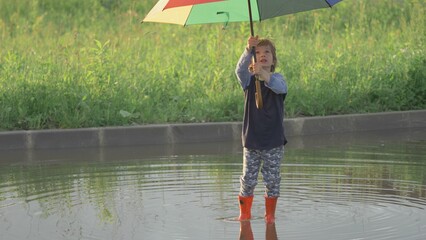 Single play and walk in puddle, boy hold a rainbow colored umbrella