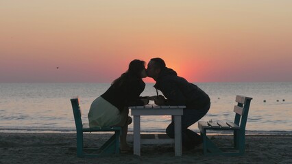 Marriage proposal, man offering engagement ring, couple sit on table on beach,