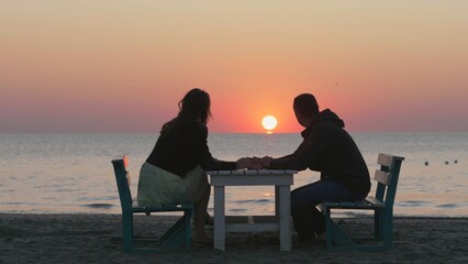 Marriage proposal, man offering engagement ring, couple sit on table on beach