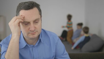 Depressed father foreground portrait focus, blurred family in background