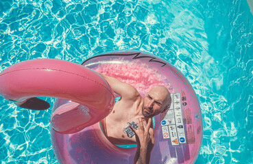 Tätowierter Mann auf einem aufblasbaren pinken Flamingo im Pool