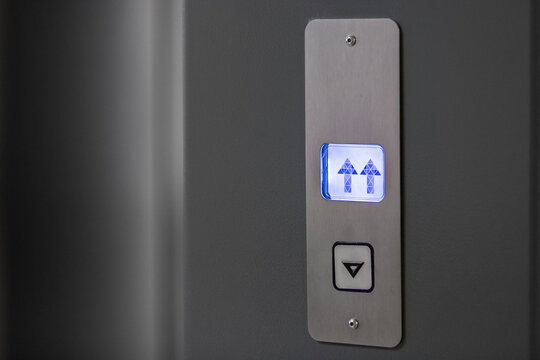Metal panel with an elevator call button and an indicator of the direction of movement of the elevator car in blue