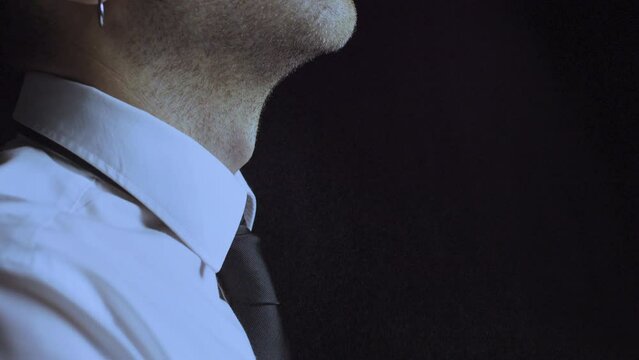 White caucasian male spraying perfume or deodorant on his neck. Handsome business man using fragrance or cologne before a meeting wearing a white shirt and black tie. Dark room background.