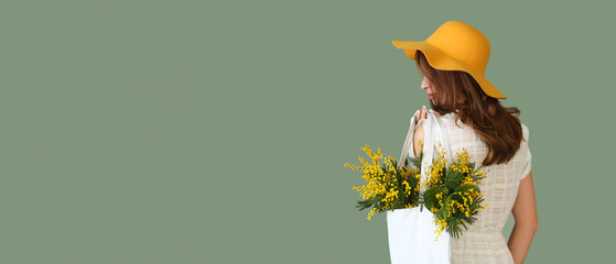 Pretty young woman holding bag with mimosa flowers on green background with space for text