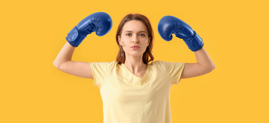 Young woman in boxing gloves on yellow background. Concept of feminism