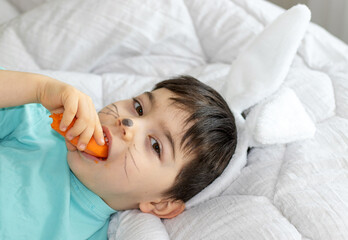 adorable kid baby boy toddler infant lies lying on bed chewing carrot or holding smartphone.painted...
