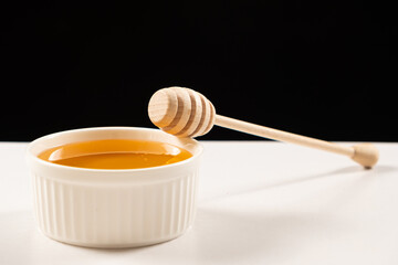 Honey in a white ceramic bowl with a wooden spoon, a place for text on a black background. Linden honey.