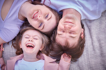 Top view of beautiful young parents, their cute little daughter. Looking at camera and smiling.