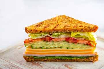 Sliced in middle high closed sandwich with wholemeal bread, cheese, ham, tomatoes, cucumber and letuce salad leaves