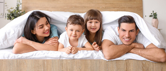 Happy family lying under blanket in bedroom at home