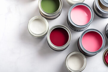Tiny sample paint cans during house renovation, process of choosing paint for the walls, different pink, magenta, green and white colors, color charts on background