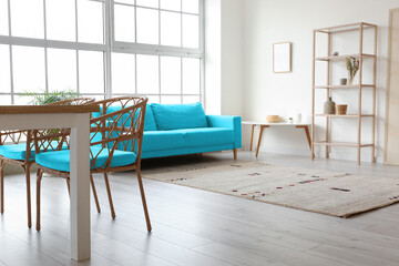 Interior of light dining room with table, wicker chairs, blue sofa and shelving unit