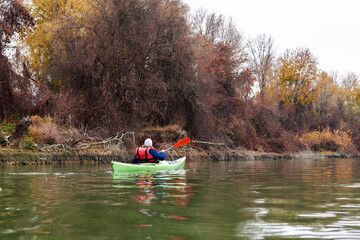 Woman rowing on green kayak on a Danube river near autumn trees