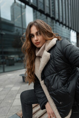 Obraz premium Fashion beautiful girl in trendy winter clothes with vintage knitted beige sweater and jacket posing in the city near the office building