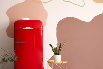 Stylish retro fridge and table with houseplants near color wall
