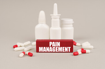 On a gray surface are pills, white jars and a red wooden block with the inscription - Pain management