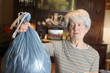 Senior woman holding stinky garbage plastic bag 