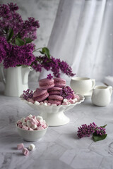Vertical composition. A bouquet of lilacs and a vase with macaroons. A concept of holidays and wishes of good morning. 