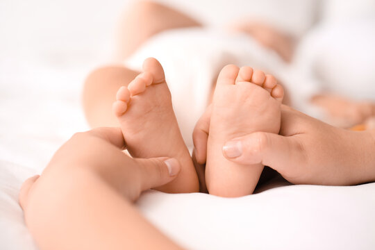 Mother massaging her baby's feet in bedroom, closeup