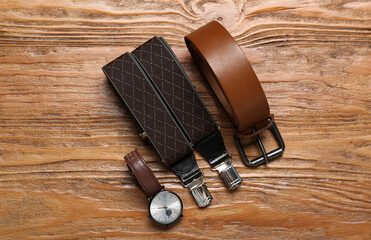 Male wristwatch, suspenders and leather belt on wooden background