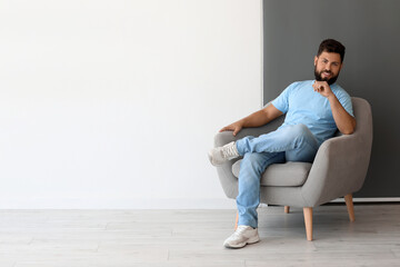 Handsome man sitting in armchair near black and white wall