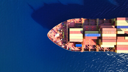Aerial drone top down photo of huge container ship full of colourful containers cruising deep blue open ocean sea
