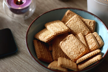 Notebook, pen, tablet, reading glasses, books, phone, candle, bowl of biscuits and cup of tea on the table. Selective focus.