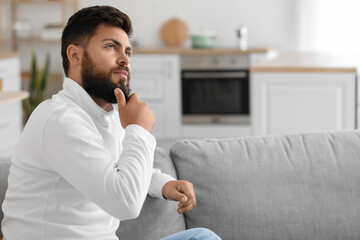 Thoughtful young bearded man on sofa in kitchen