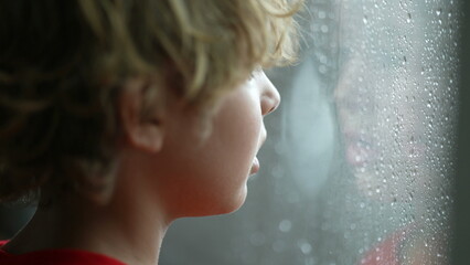 Young boy standing by window during cold rainy day wanting to go outside