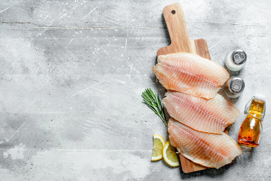 Fish fillet on a cutting Board with lemon slices, spices and oil in a bottle.
