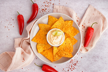 Plate with tasty nachos and chipotle sauce on light background