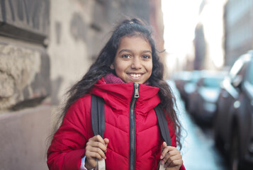 Fototapeta premium portrait of little girl with backpack on her shoulder on the street