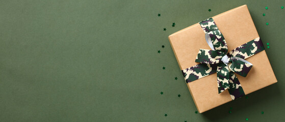 Gift box, tied with a ribbon bow in military colors on green background with copy space. Defender of the Fatherland Day or Veterans Day banner design.