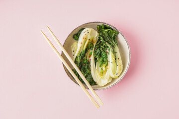 Bowl of tasty stewed pak choi cabbage and chopsticks on pink background