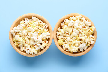 Wooden bowls of tasty popcorn on color background