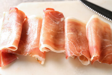 Board with rolled slices of delicious ham, closeup