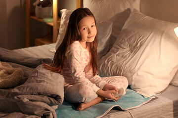 Little girl sitting on electric heating pad in bedroom at night