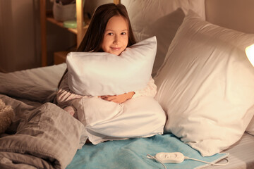 Little girl with pillow sitting on electric heating pad in bedroom at night © Pixel-Shot