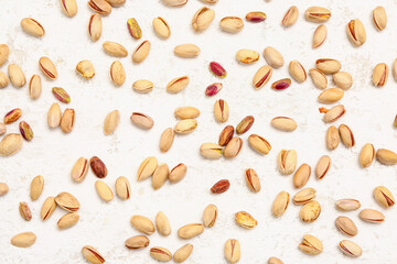 Many tasty pistachio nuts scattered on white background