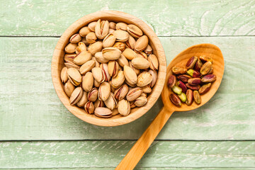 Spoon and bowl with tasty pistachio nuts on green wooden background