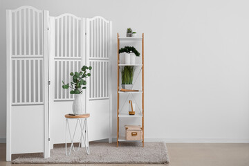 Interior of room with folding screen, shelving unit and houseplants near white wall