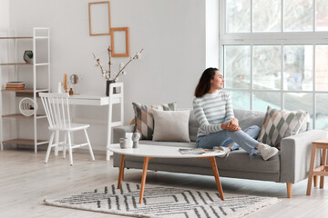 Young woman sitting on grey couch in living room