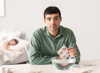 Young man dipping mustard plaster into bowl of water in bedroom