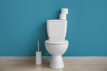 Ceramic toilet bowl, brush and paper rolls near blue wall