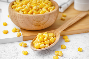Cutting board with spoon and bowl of canned corn kernels on white table