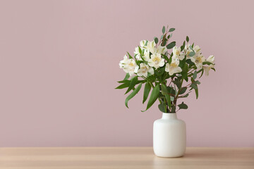 Vase with beautiful alstroemeria flowers on table against color wall